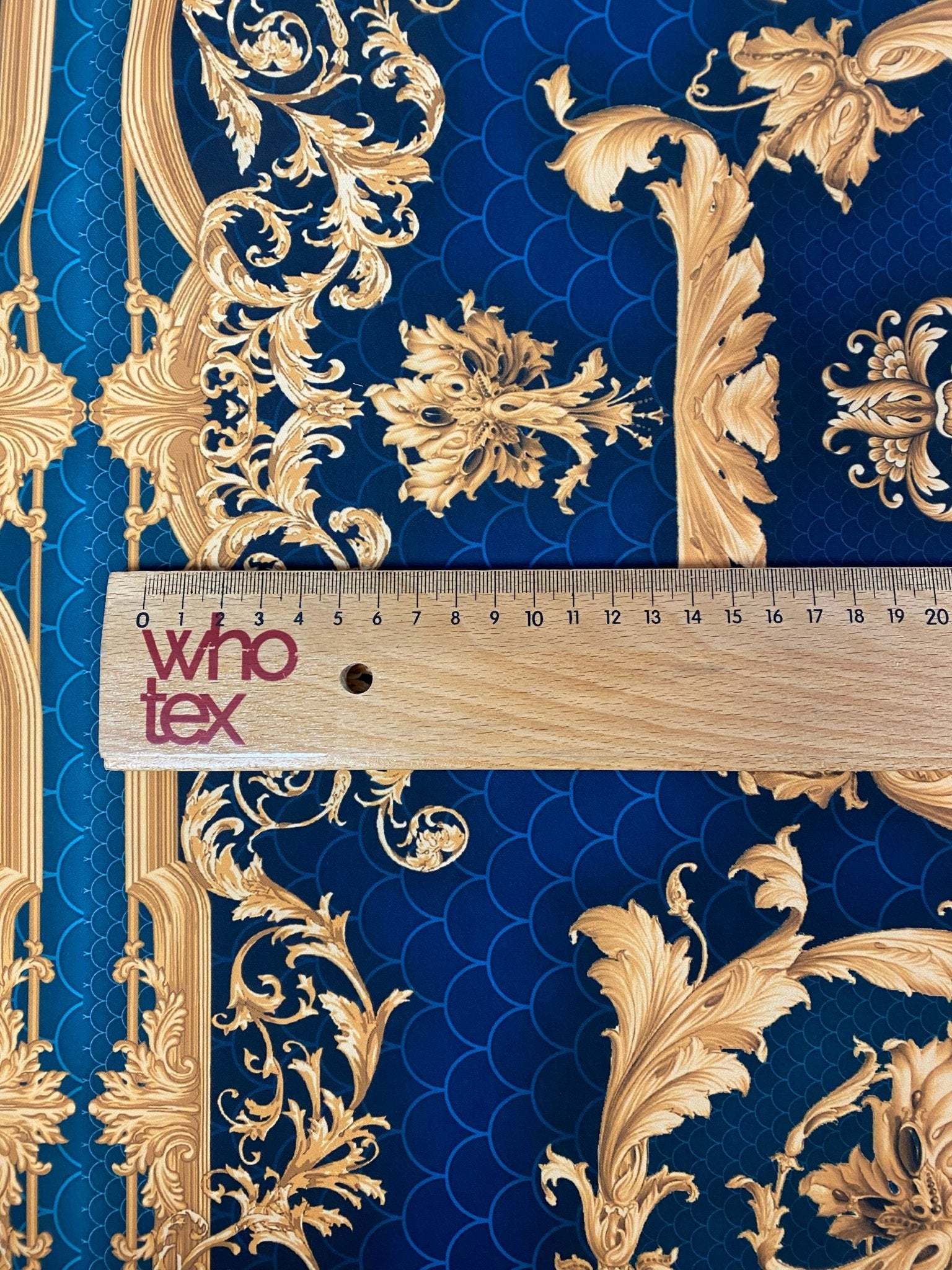 Vintage peacock pattern fabric with intricate gold designs on a deep blue background and a ruler for scale